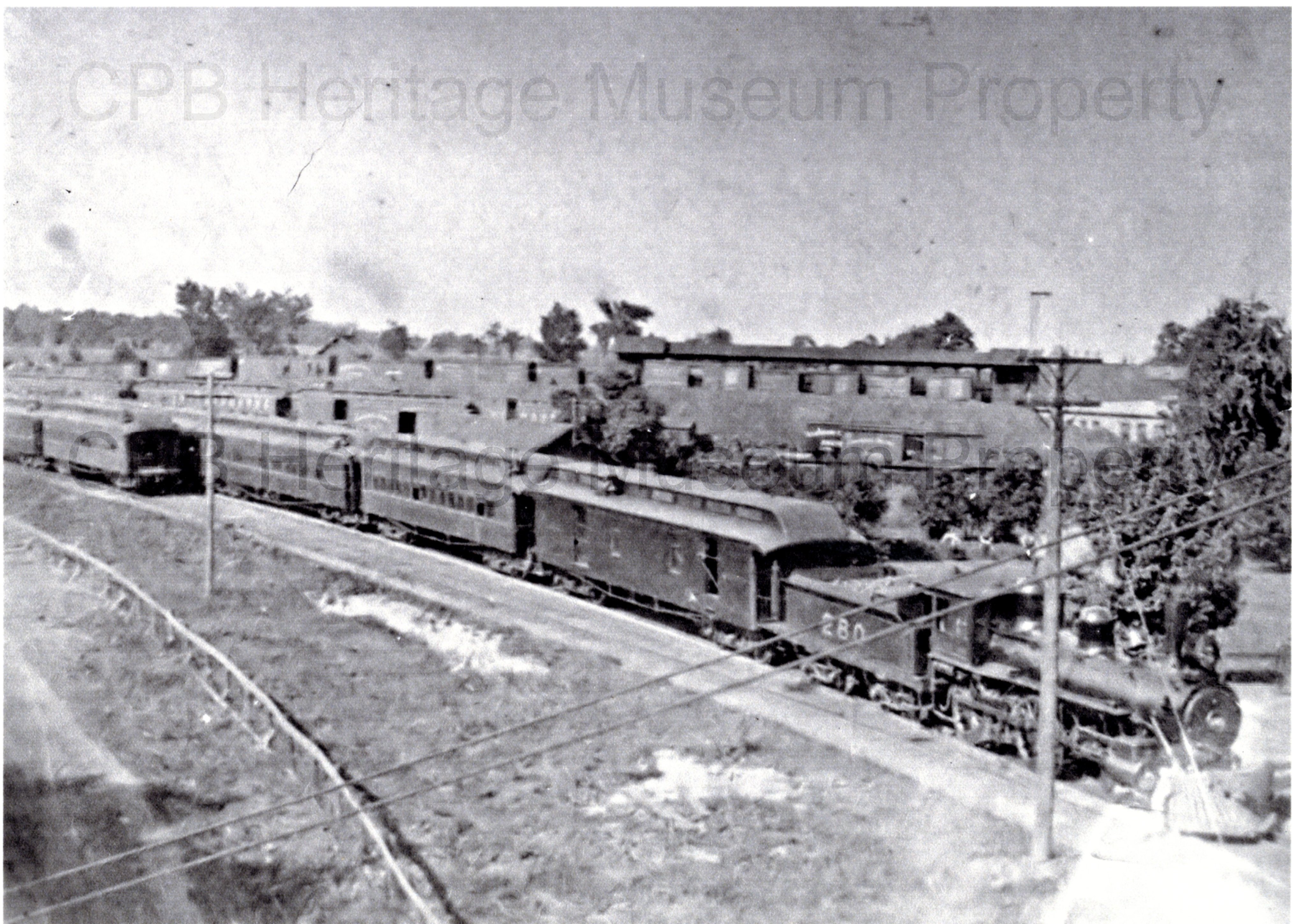 Black and white photograph of train yards. There is a train visible on tracks in the center.