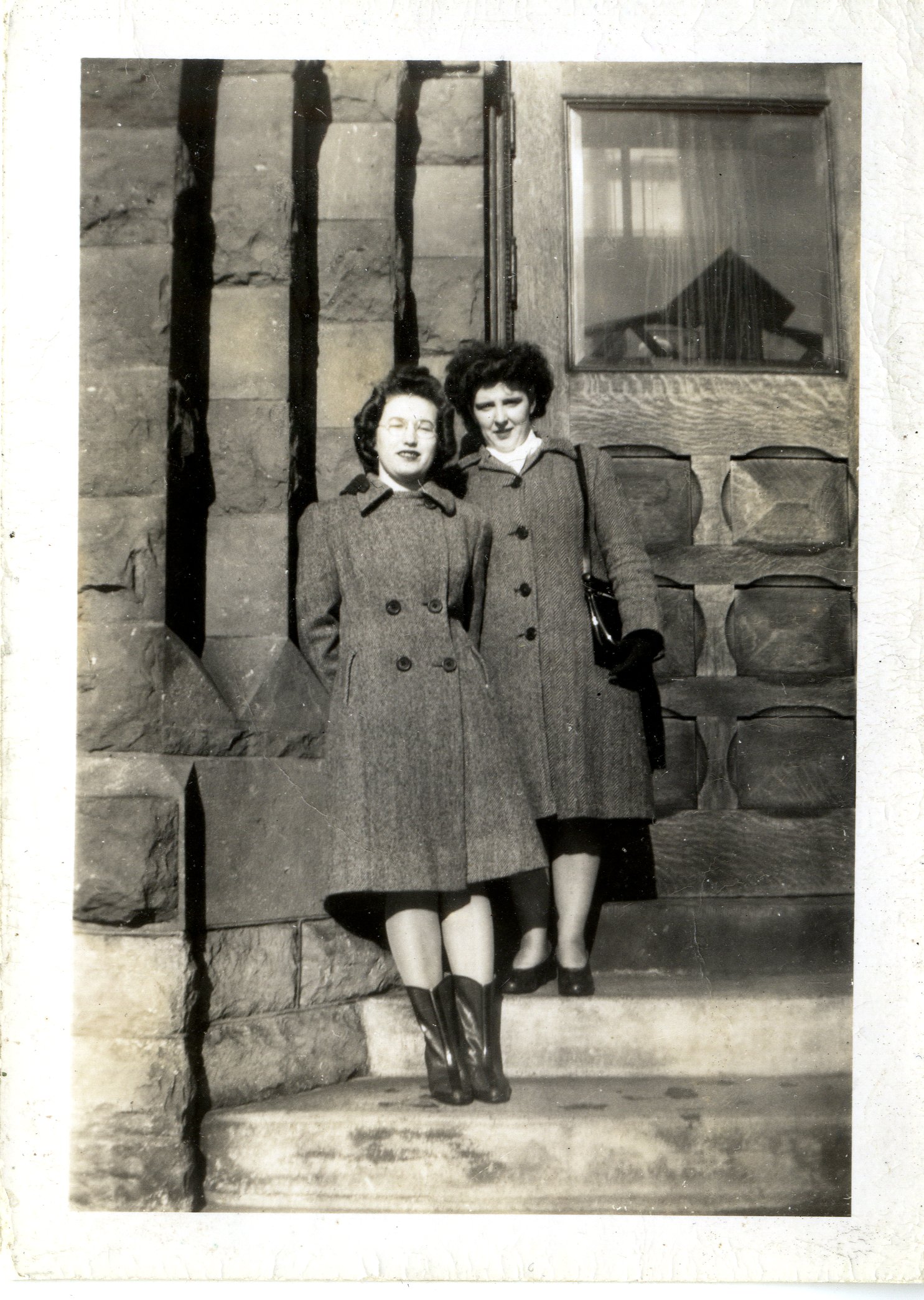 Black and white photograph of Jean Cook (Dickens) and Doreen McDiarmid (Simpson?) wearing long grey coats with boots to their calves standing on the front steps of the Town Hall in Carleton Place.