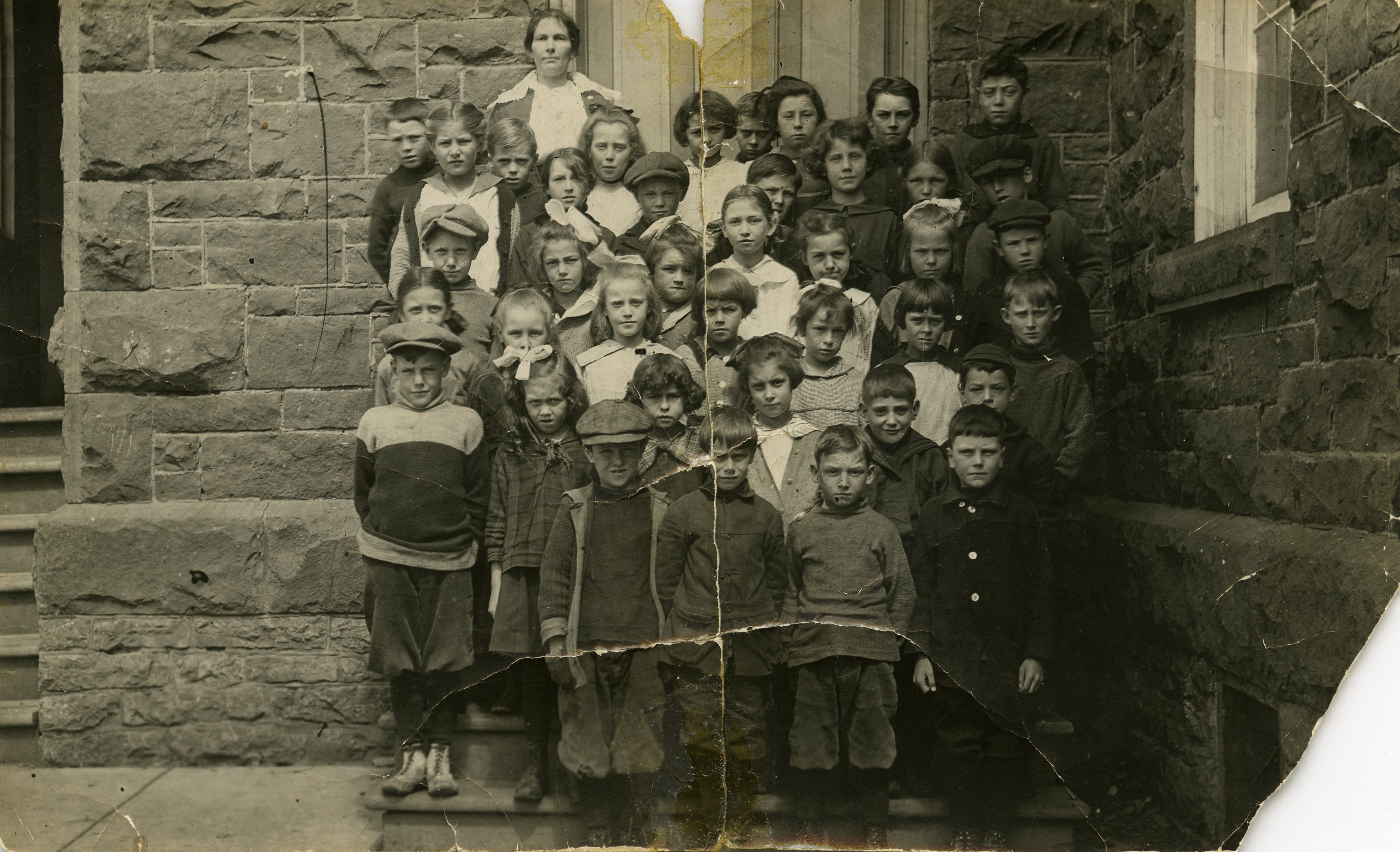 Black and white photograph of group of school children and teacher posing outside school.