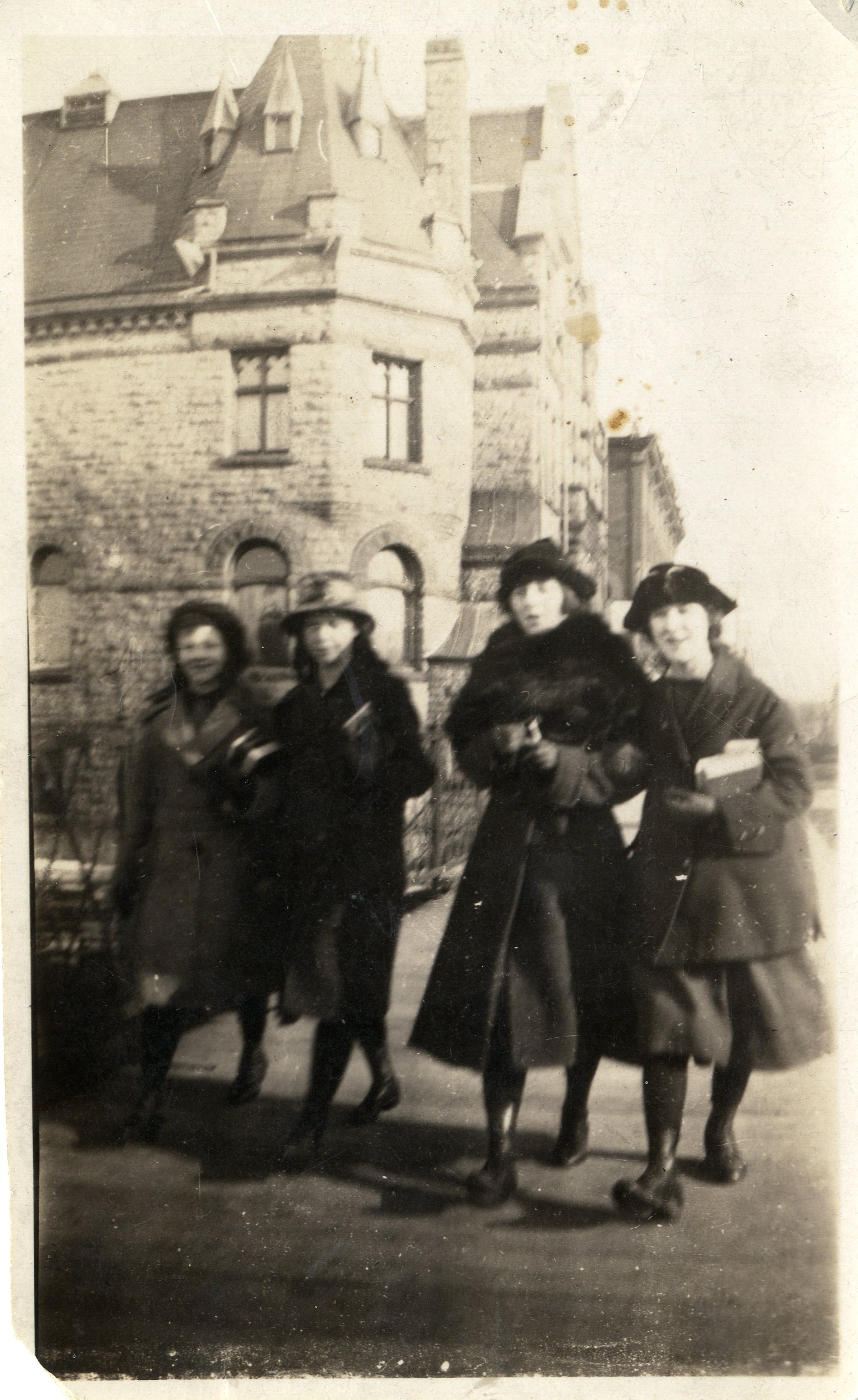 Sepia-toned photograph of four women walking across bridge in front of Town Hall in Carleton Place. They are all wearing coats, hats, and carrying books. Armistice Day, November 11, 1918. Written on reverse: "Leita Andison , Annie ?, Flora Ormrod, Bessie Harrod Armistice Day" Black and white reprint included in envelope.