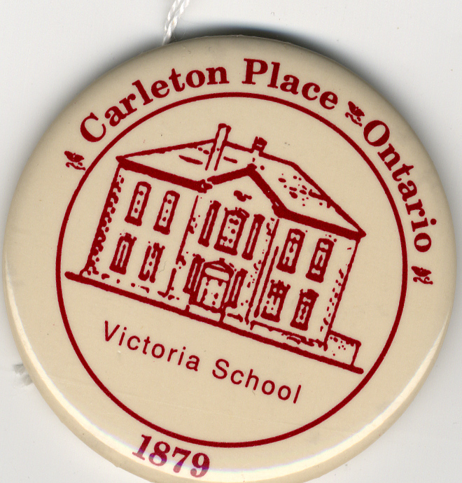 Circular plastic button, red lettering on beige discolored white background: "Carleton Place Ontario, Victoria School, 1879". Metal pin on reverse.