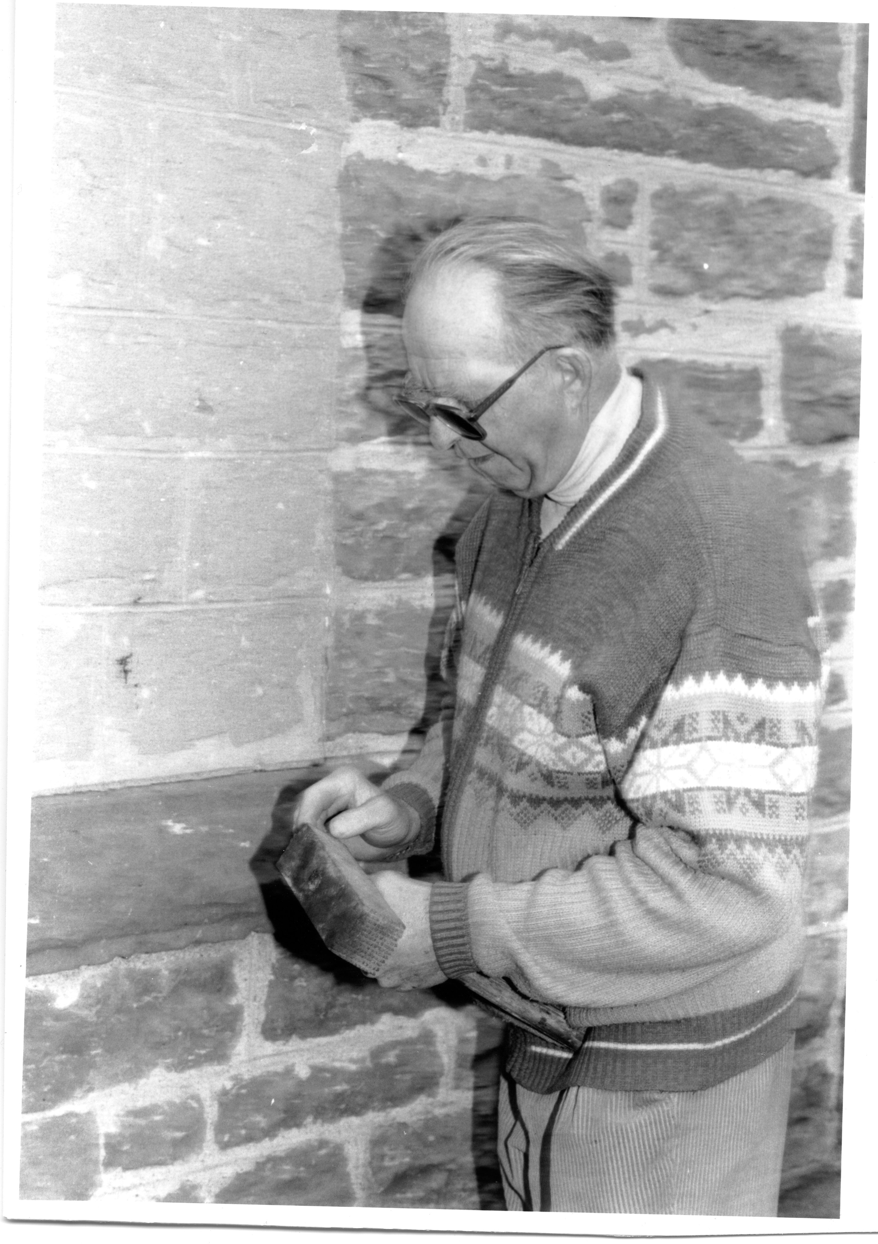 Black and white photograph of a white man with grey hair holding a bushing hammer. 