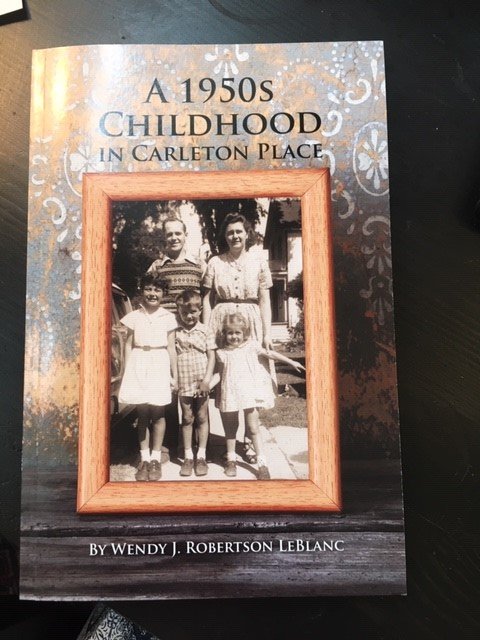 Rectangular book with soft covers, glue binding. Image of Robertson family (Ken, Betty, Wendy, Wayne, Kathryn) taken in 1954 on front cover. "A 1950s Childhood in Carleton Place by Wendy J. Robertson Leblanc". Black and white photo of family on cover with outline of contents on back cover. Signed in ink on first page by the author. Outlines Wendy's childhood growing up at 285 James Street in Carleton Place, attending Victoria and Central Schools, her father working at Findlays, mother at Leigh Instruments.